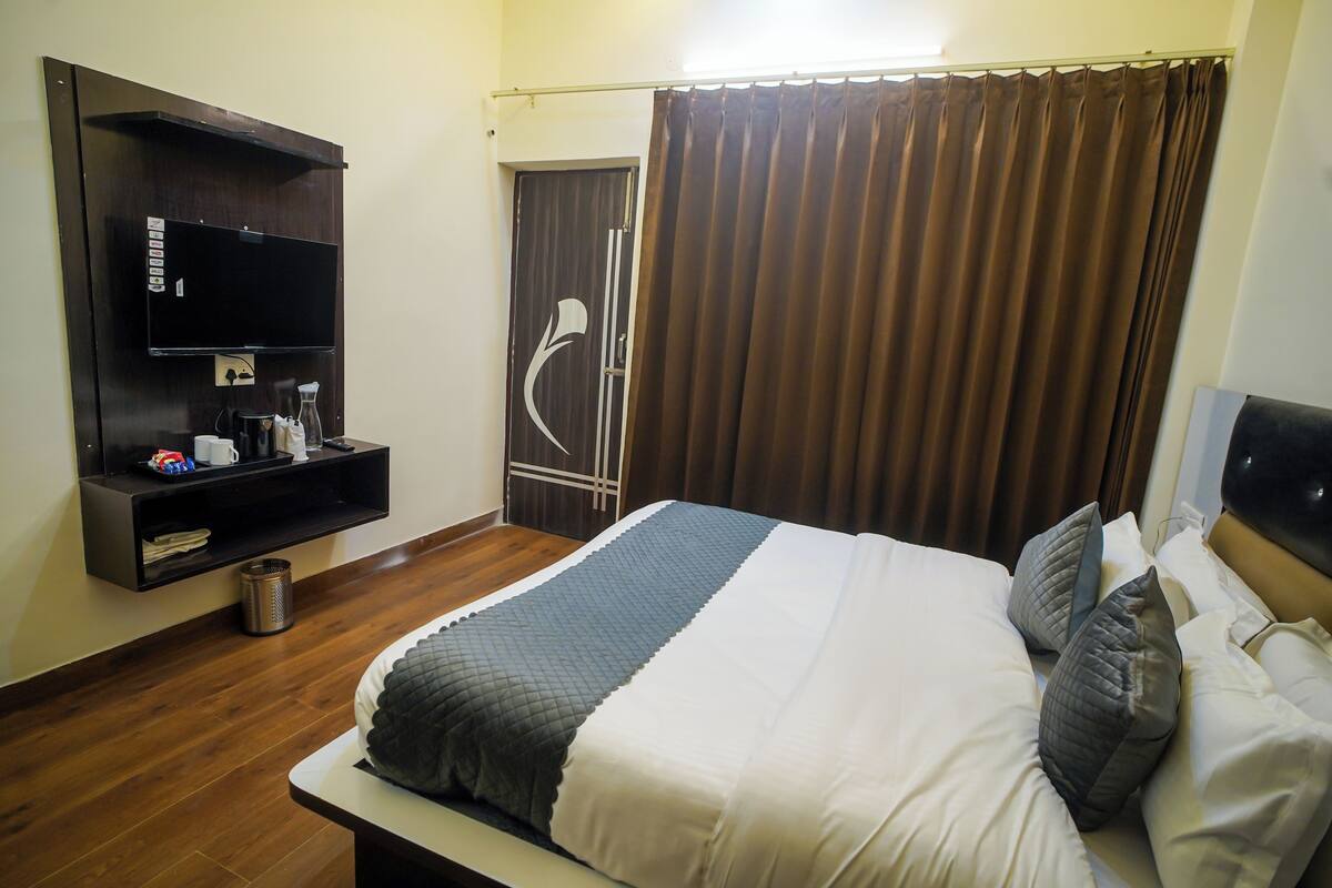 Ein Hotelzimmer mit Bett, einem an der Wand befestigten Fernseher, einer kleinen Ablage mit Gegenständen und einem Vorhang.
