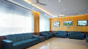 A modern waiting area with blue sofas, wooden panel walls, ceiling fans, and large windows. - Uno Premium Dalhousie (Dalhousie)