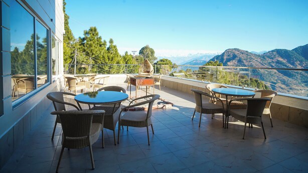 A terrace with wicker furniture and a table, overlooking a mountainous landscape. - Uno Premium Dalhousie (Dalhousie)