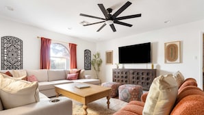 A modern living room with a sofa, ottomans, a coffee table, and a flat-screen TV.