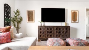 A living room with a white sofa, patterned ottomans, a wooden coffee table, a TV, and a decorative cabinet.