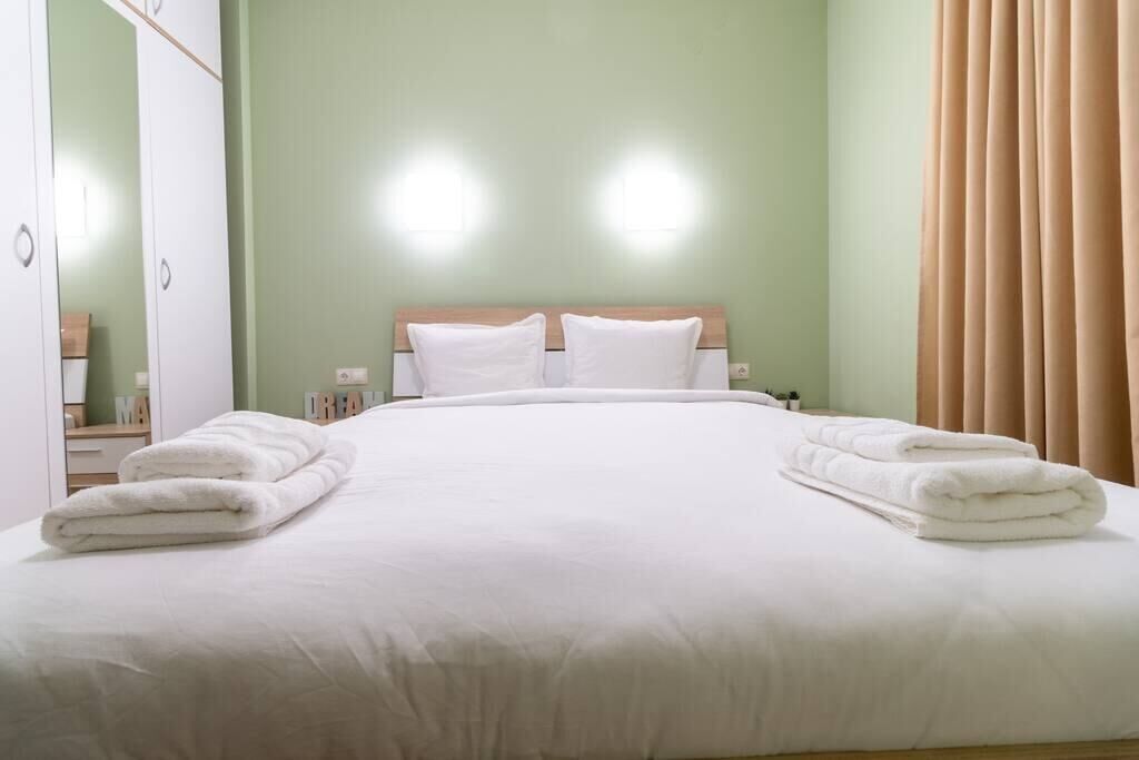 A neatly made bed with white linens and towels, a wooden headboard, and a green wall.