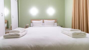 A neatly made bed with white linens and towels, a wooden headboard, and a green wall.