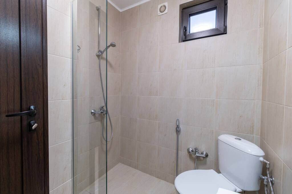 A bathroom with a glass shower enclosure, a toilet, and a small window above the toilet.
