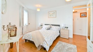A bedroom with a bed, bedside tables, a nightstand, a mirror, a window with curtains, and a door.