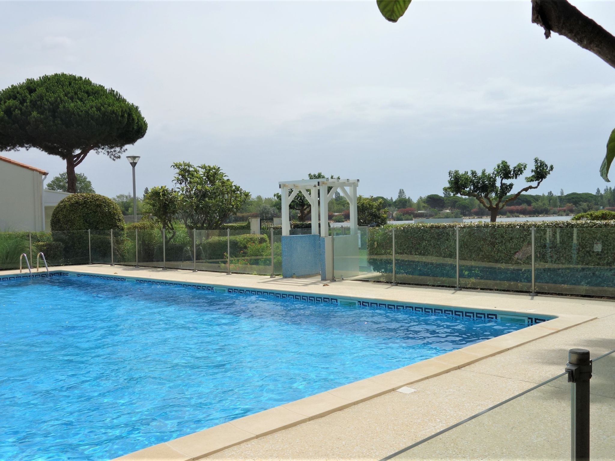 Una piscina con agua cristalina azul, rodeada por una valla y una estructura tipo pabellón al fondo.