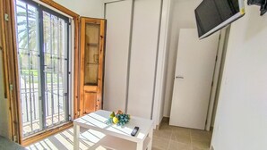 Et værelse med en skydedør til en balkon, et hvidt bord med en fjernbetjening og et ophængt fjernsyn på væggen.