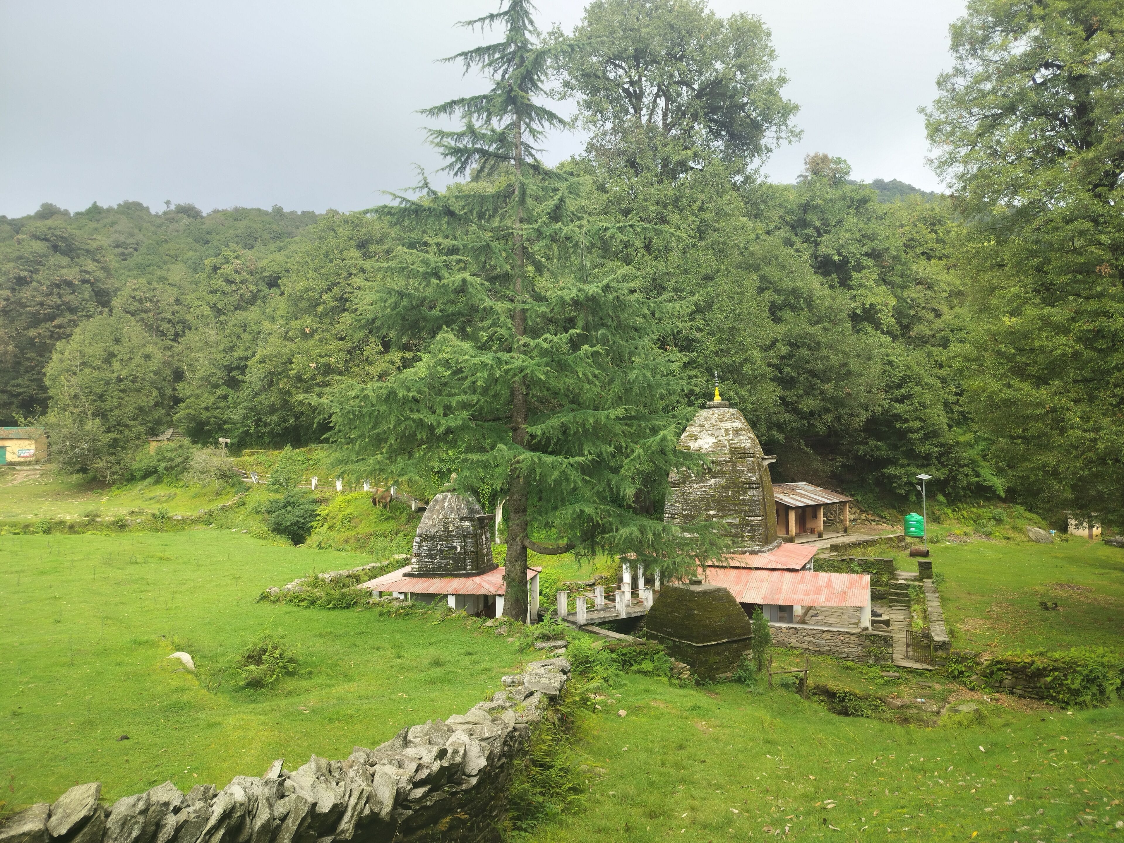 A traditional temple complex with stone structures, surrounded by lush greenery and a stone wall.