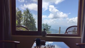 A chessboard on a table with a view of trees and mountains through a window.