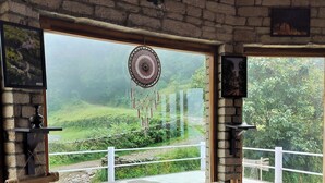 A cozy room with a large window overlooking a lush landscape, a dreamcatcher decoration, and a wooden table.