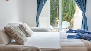 Een slaapkamer met een bed, kussens, een raam met gordijnen en uitzicht op groen.