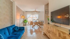 Een moderne woonkamer met een blauwe bank, een tv-meubel van hout, en een eethoek met stoelen en een tafel.