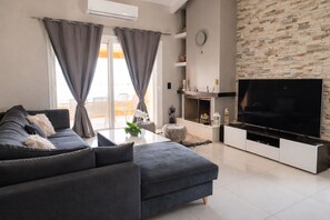 Un salon moderne avec un canapé gris, un téléviseur à écran plat, une cheminée et un mur en pierre.
