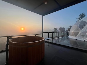 A wooden hot tub on a balcony with a view of the sunrise.
