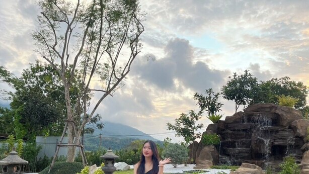 A woman sitting on a wooden deck by a pond with a waterfall and trees in the background. - yugencamping (Khao Kho)