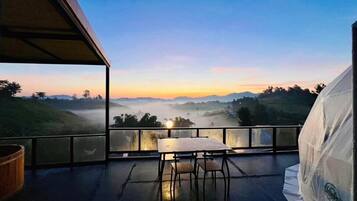 A balcony with a table and chairs, overlooking a misty landscape during sunrise or sunset.