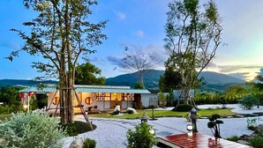 A traditional Japanese-style building with a wooden deck, surrounded by a landscaped garden with rocks and trees. - yugencamping (Khao Kho)
