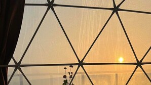 A room with a large window featuring a geometric pattern, a small table with a vase of flowers, and two cushioned seating areas. - yugencamping (Khao Kho)