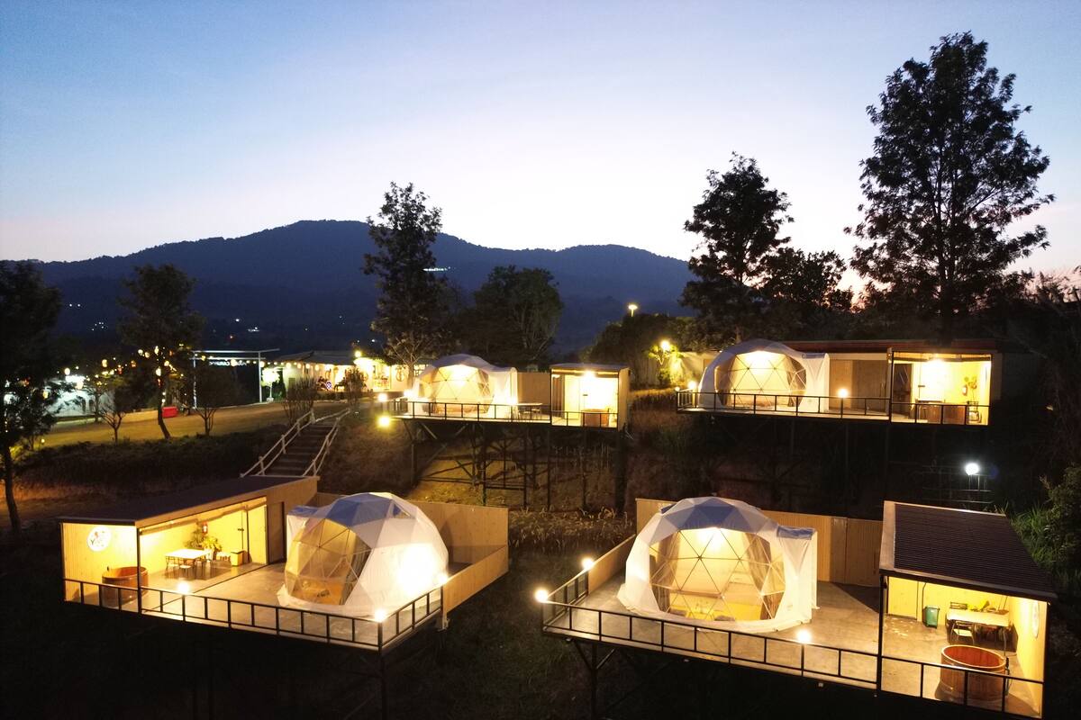 A series of dome-shaped accommodations with outdoor seating areas, connected by walkways, set against a mountainous backdrop.