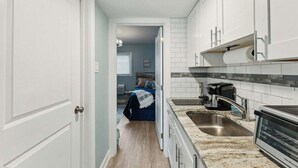 Una cocina estrecha con gabinetes blancos, un lavamanos de acero inoxidable y un horno empotrado.