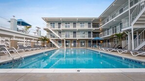 Una piscina con sillones de descanso y un edificio de varios pisos con balcones.
