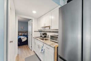 A compact kitchen with white cabinets, a stainless steel refrigerator, a sink, and a toaster.