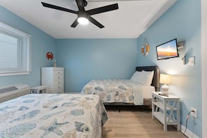 A bedroom with two beds, a ceiling fan, a TV, and a wall-mounted heater.