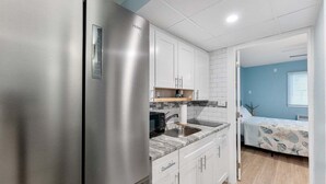 A compact kitchen with a stainless steel refrigerator, white cabinets, a marble countertop, and a small sink.