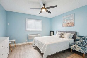 A bedroom with a bed, a ceiling fan, a window with blinds, a radiator, a dresser, and a chair.