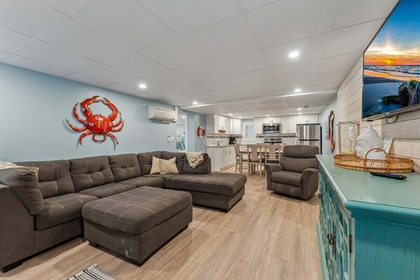 A modern living room with a sectional sofa, a small armchair, a dining area, and a kitchen in the background.