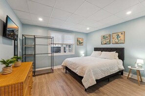 A bedroom with a bed, a window, a wall-mounted TV, and artwork.