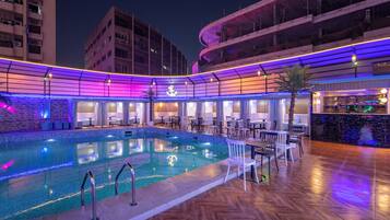 A pool area with a curved roof, lounge chairs, and a bar area.