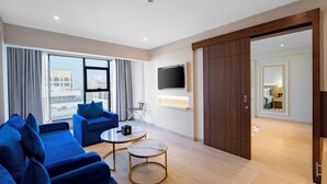 Een moderne hotelkamer met een groot raam, een flatscreen televisie, een bank, een salontafel en een kledingkast.
