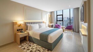 Een moderne hotelkamer met een groot bed, een bureau met telefoon, een stoel en uitzicht op de stad.