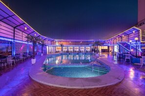 An indoor swimming pool with a tiled edge, surrounded by seating areas and a covered walkway. - Grand Ambassador Hotel (Dubai)