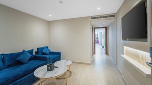 Een moderne woonkamer met een blauwe bank, een marmeren salontafel en een aan de muur bevestigde televisie.