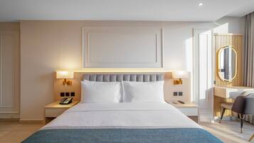 A modern hotel room with a large bed, bedside lamps, a desk with a chair, and a mirror.