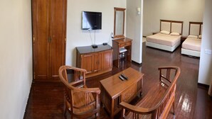 A room with a wooden desk, a television, a wardrobe, a bed, and a ceiling fan.