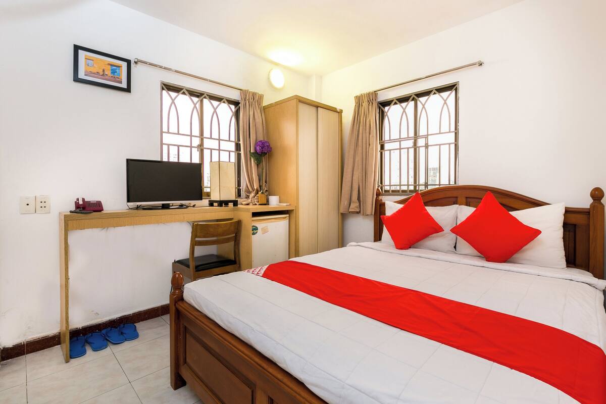 Een slaapkamer met een bed, een bureau met een computer, een kledingkast en een raam met gordijnen.