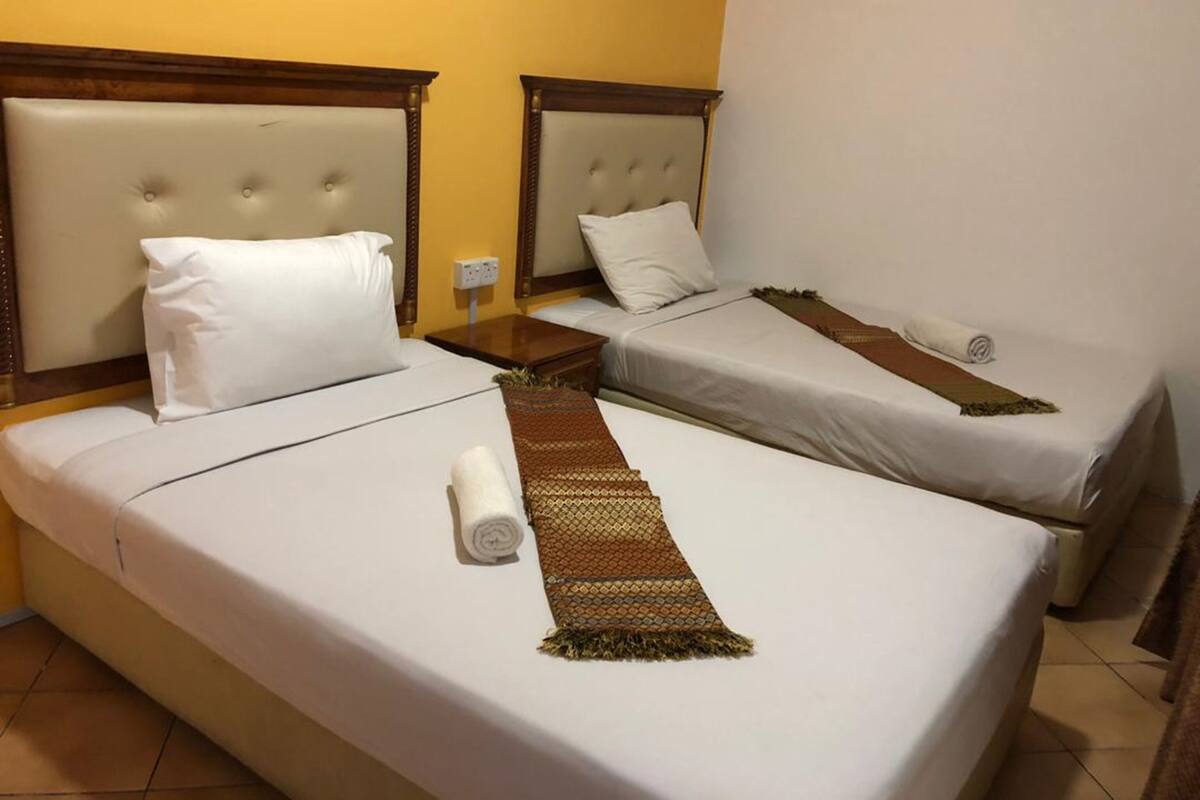 Een hotelkamer met twee bedden, elk met een houten hoofdbord, witte lakens en een bruine decoratieve plaid.