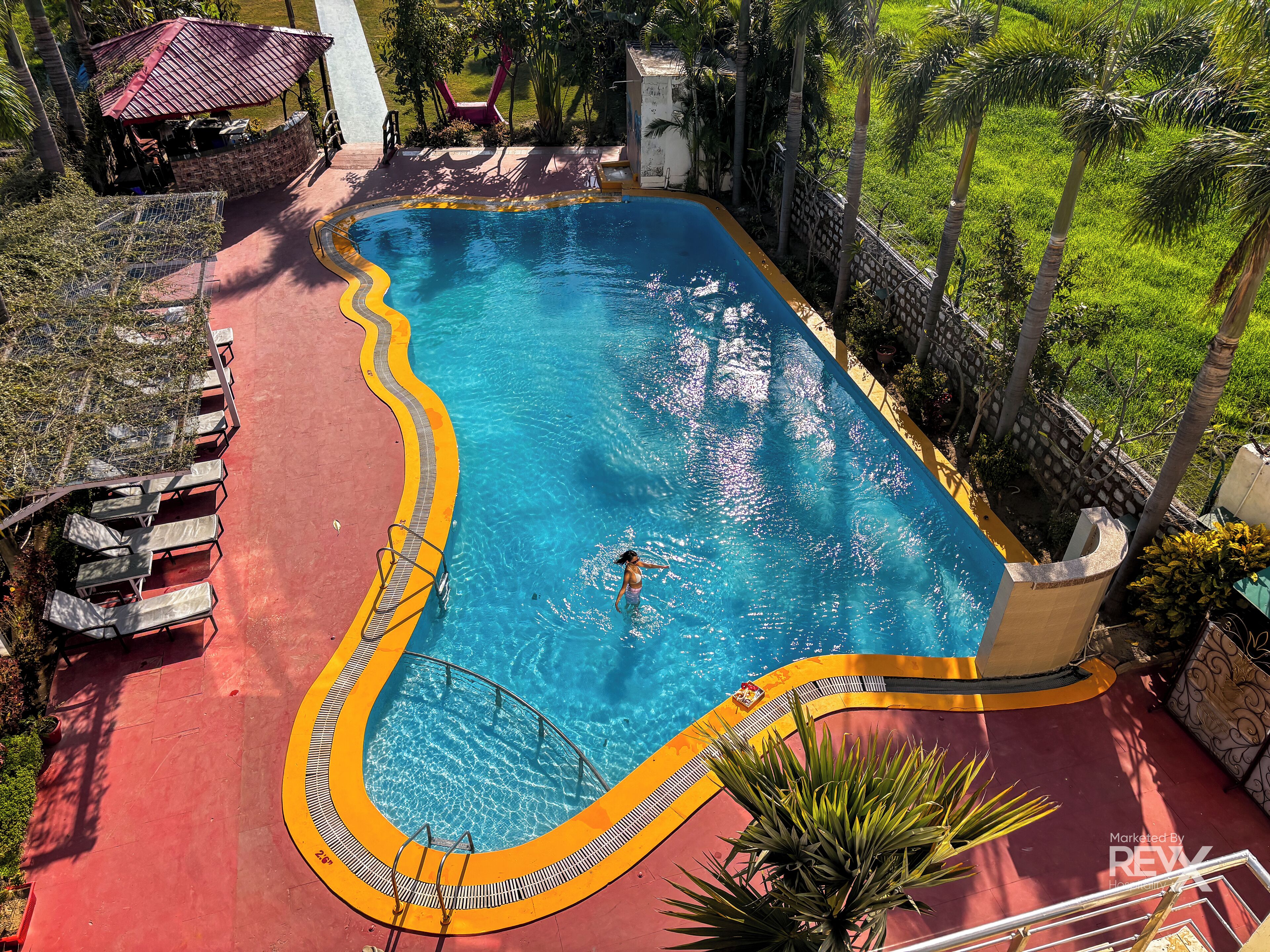 A rectangular swimming pool with a curved edge, surrounded by a red deck and a yellow safety border.