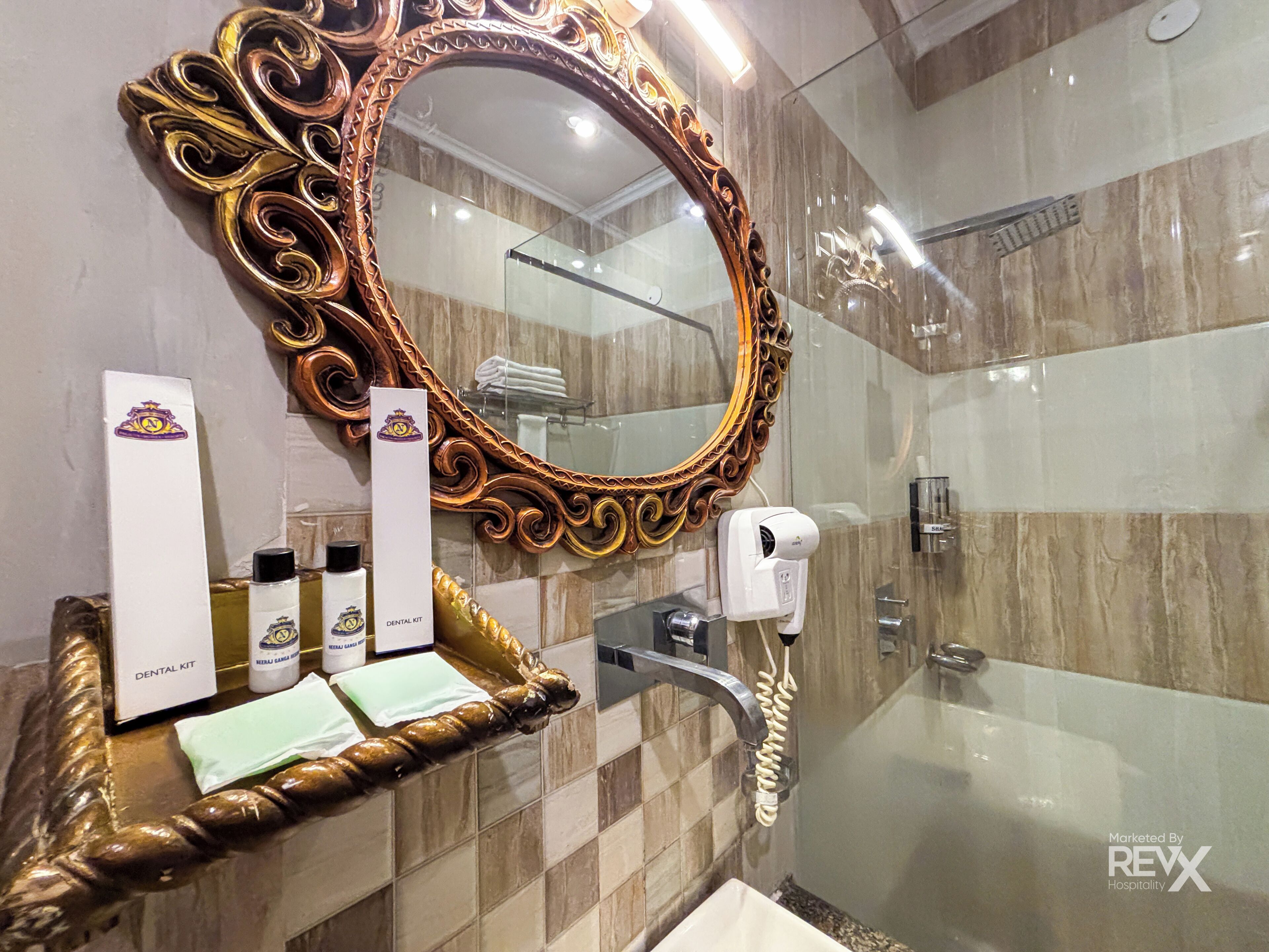 A bathroom with a large ornate mirror, a sink, a glass shower enclosure, and a dental kit on the counter.