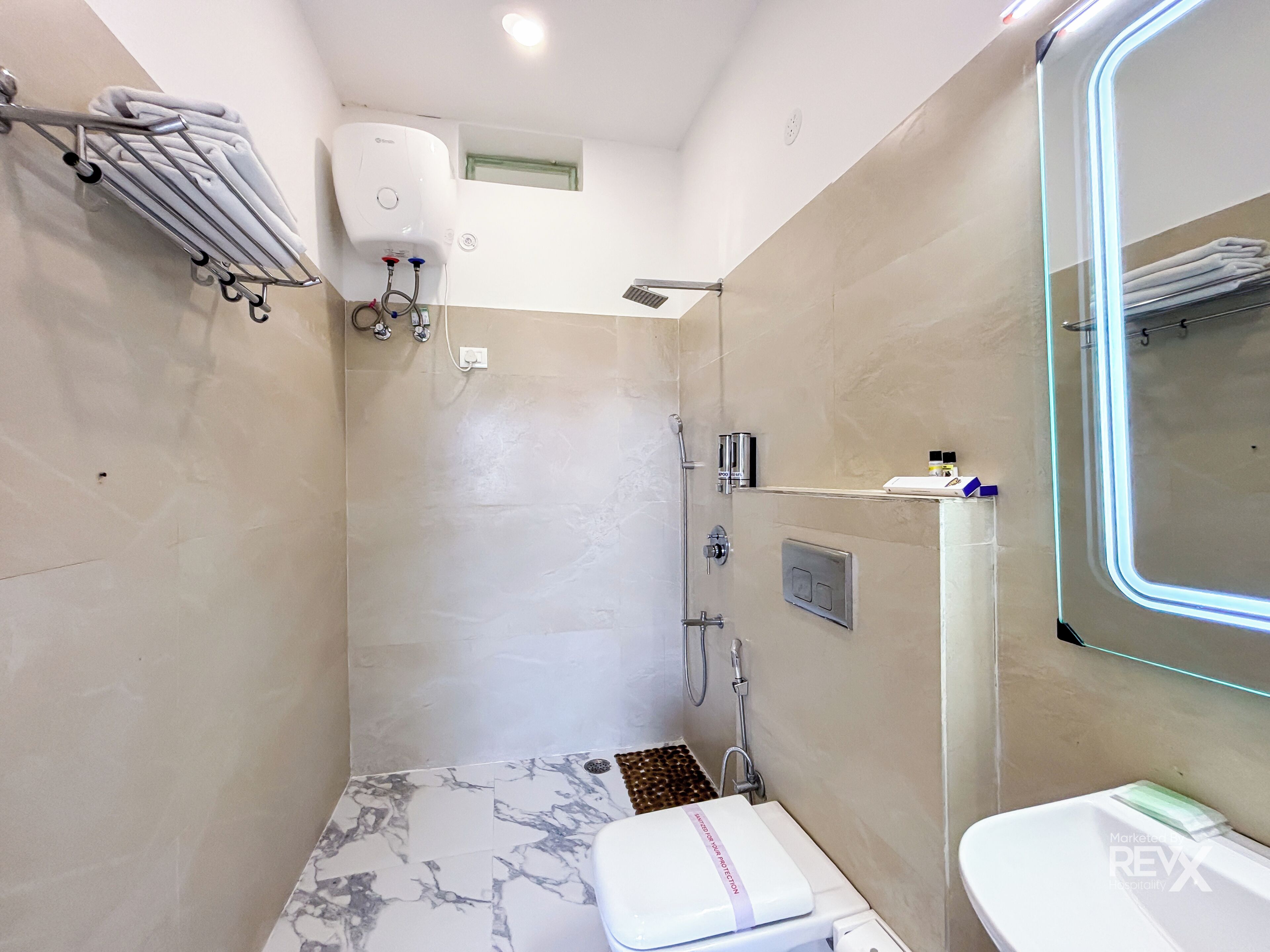 Une salle de bain moderne avec un sol en marbre, des toilettes, un espace douche doté d’un miroir encadré de verre et un porte-serviettes.