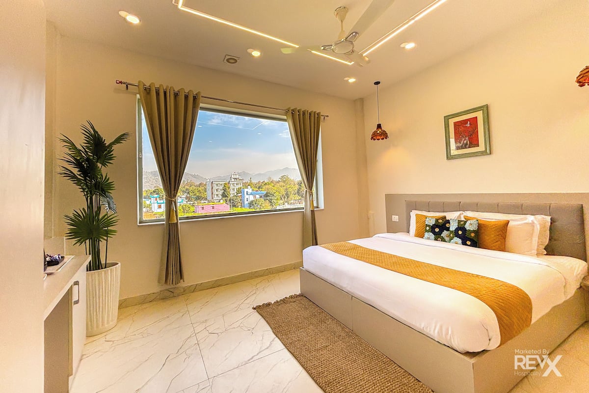 Ein Hotelzimmer mit Bett, einem Vorhangfenster, einem Deckenventilator und Blick auf Gebäude.