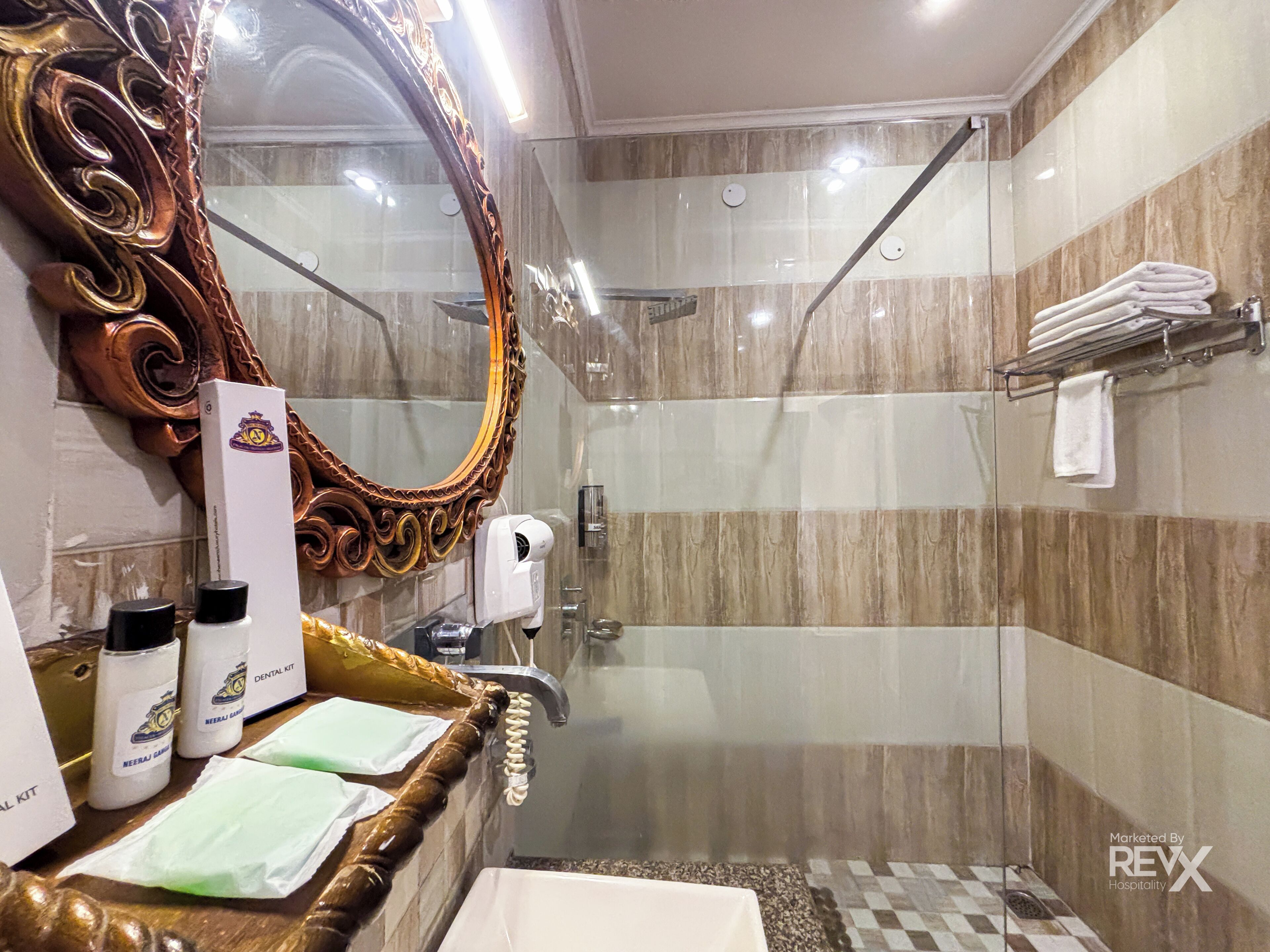 A bathroom with a large ornate mirror, a shower, a sink, and a towel rack.