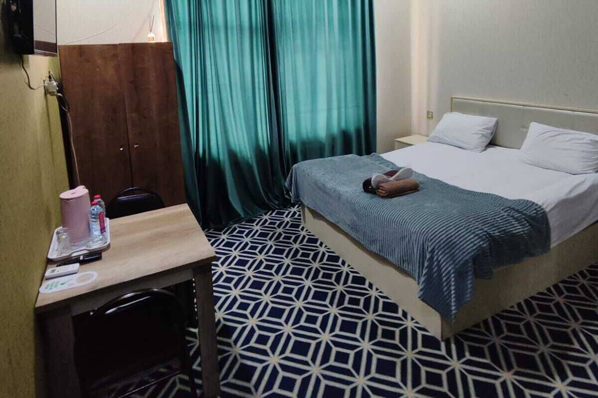 A hotel room with a bed, a desk, a chair, a mirror, and a window with curtains.