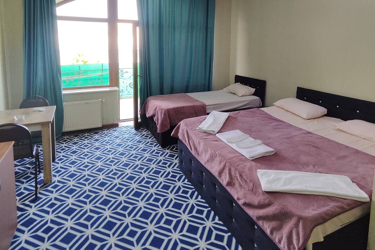 A hotel room with two beds, a desk, and a window with curtains.