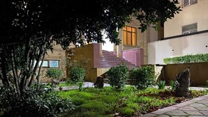 A courtyard with a stone pathway, a small garden area, and a building with a staircase. - Ekm Hotel (Baku)