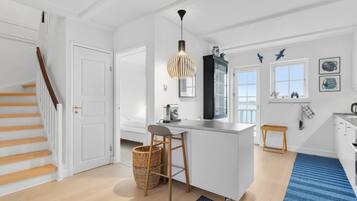 A modern kitchen with a central island, a hanging pendant light, and a view of the sea through a window.