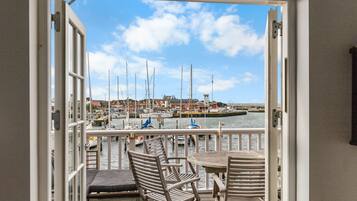 A view from a room with a wooden deck and a table and chairs, overlooking a marina with boats and buildings.